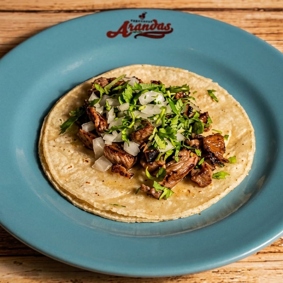 A single Arandas carne asada taco with onions and cilantro on a blue plate.