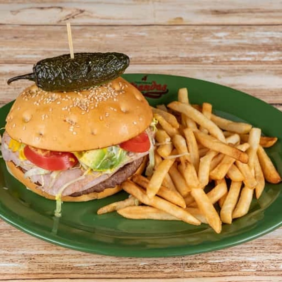 Cheeseburger topped with lettuce, tomato, onion, and a whole grilled pepper, served with fries on a green plate.
