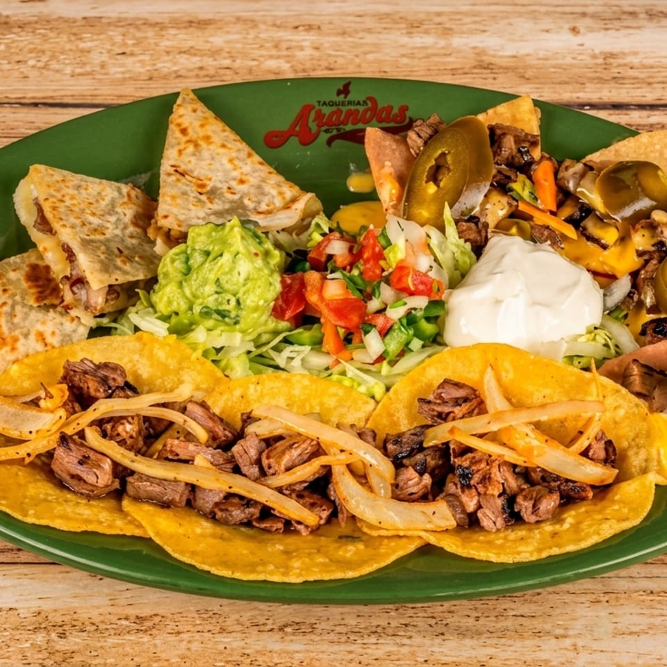 A green plate filled with tacos, quesadillas, nachos, guacamole, salsa, and sour cream.