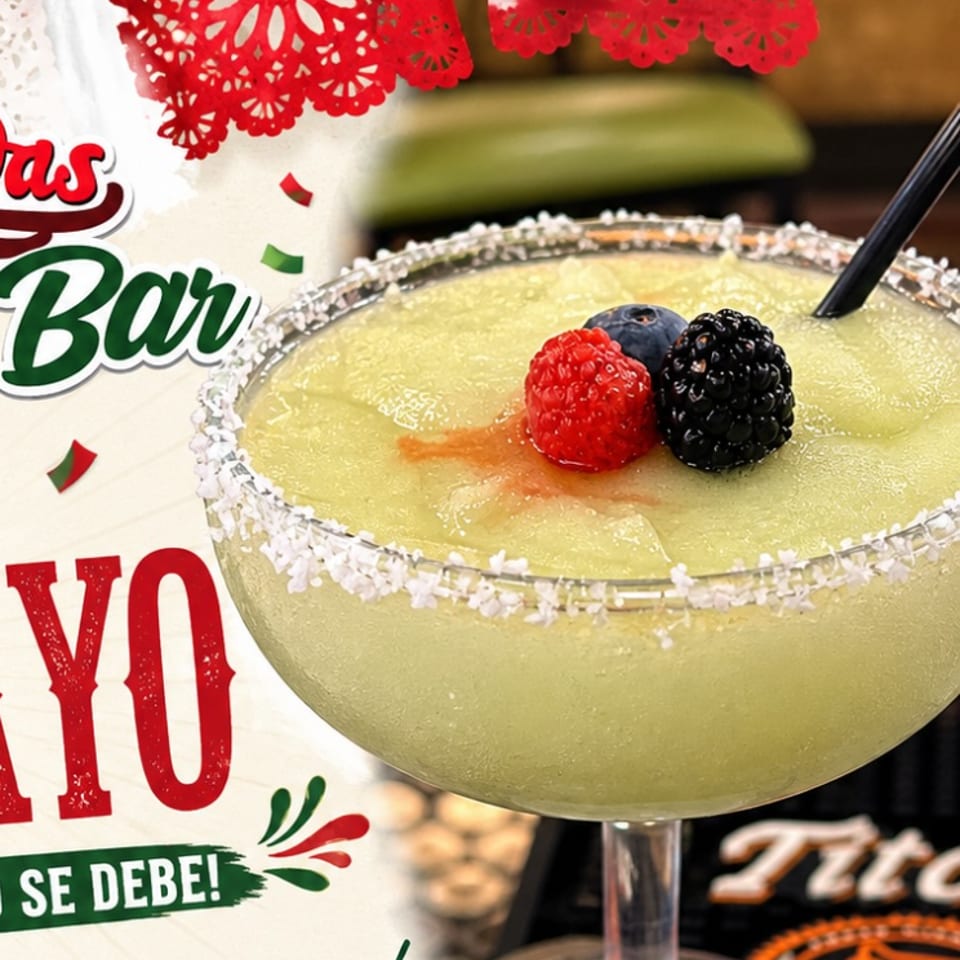 Pale green cocktail with a coconut-rimmed glass, topped with raspberries and blackberry beside festive Cinco de Mayo decorations.