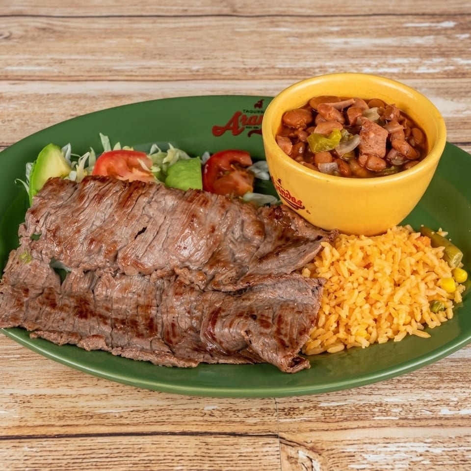 Grilled steak, rice, beans, and a side salad with avocado and tomato on a green plate.
