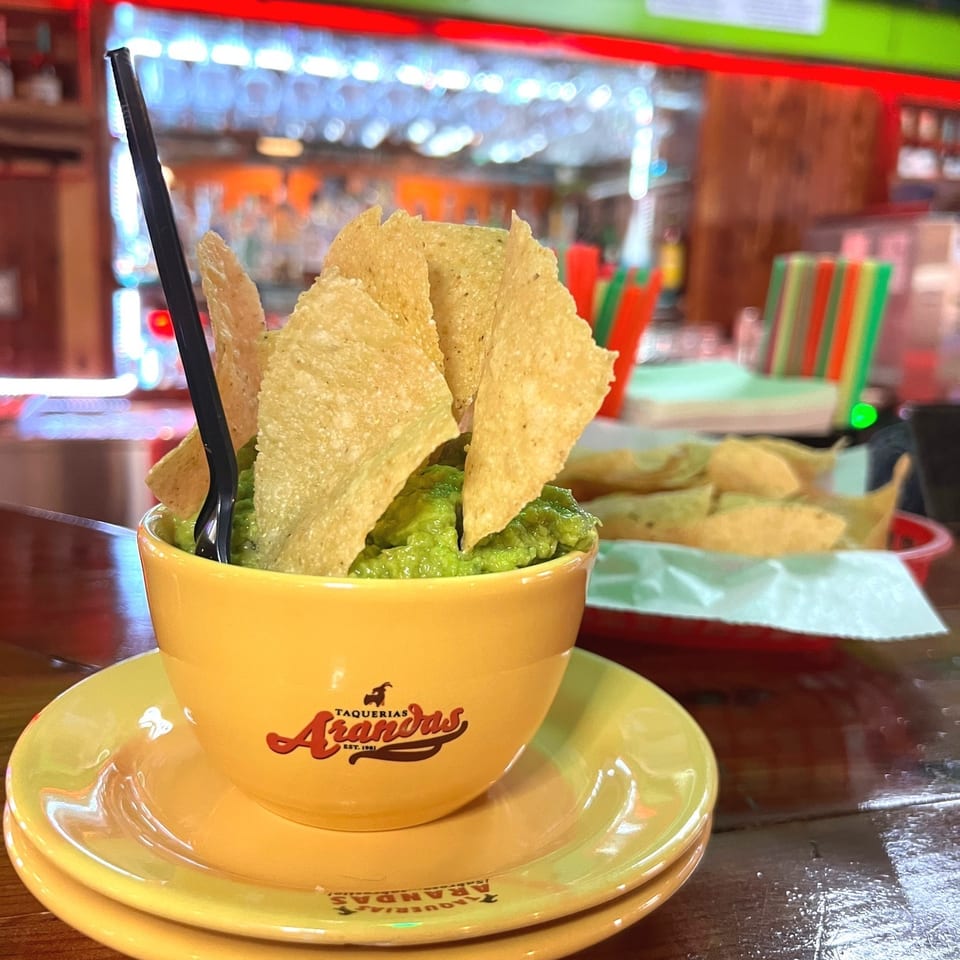 Bowl of guacamole topped with crispy tortilla chips and a black spoon at Taquerias Arandas.