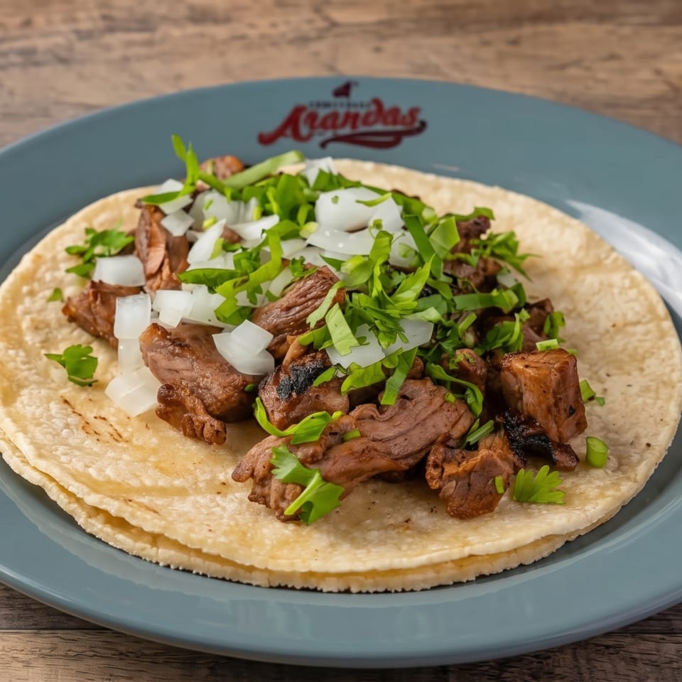 Two corn tortillas topped with grilled meat, diced onions, and fresh cilantro on a blue plate.